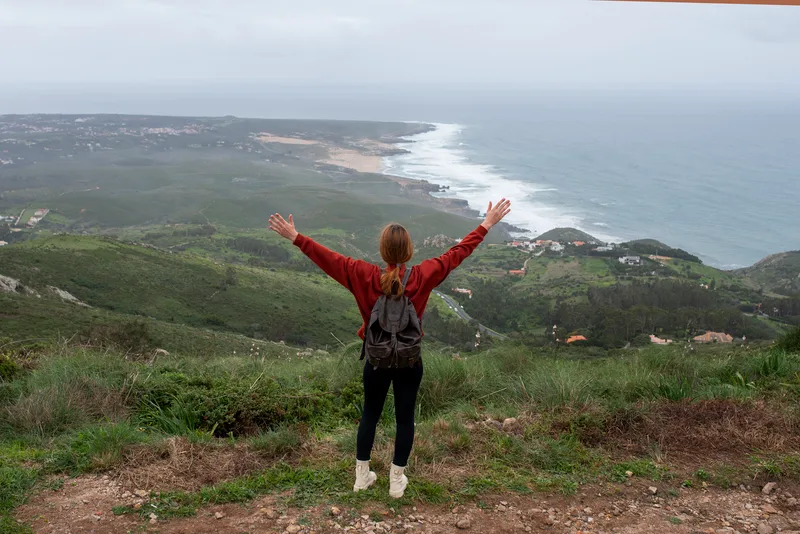 A girl who is standing on top of a mountain with her arms up